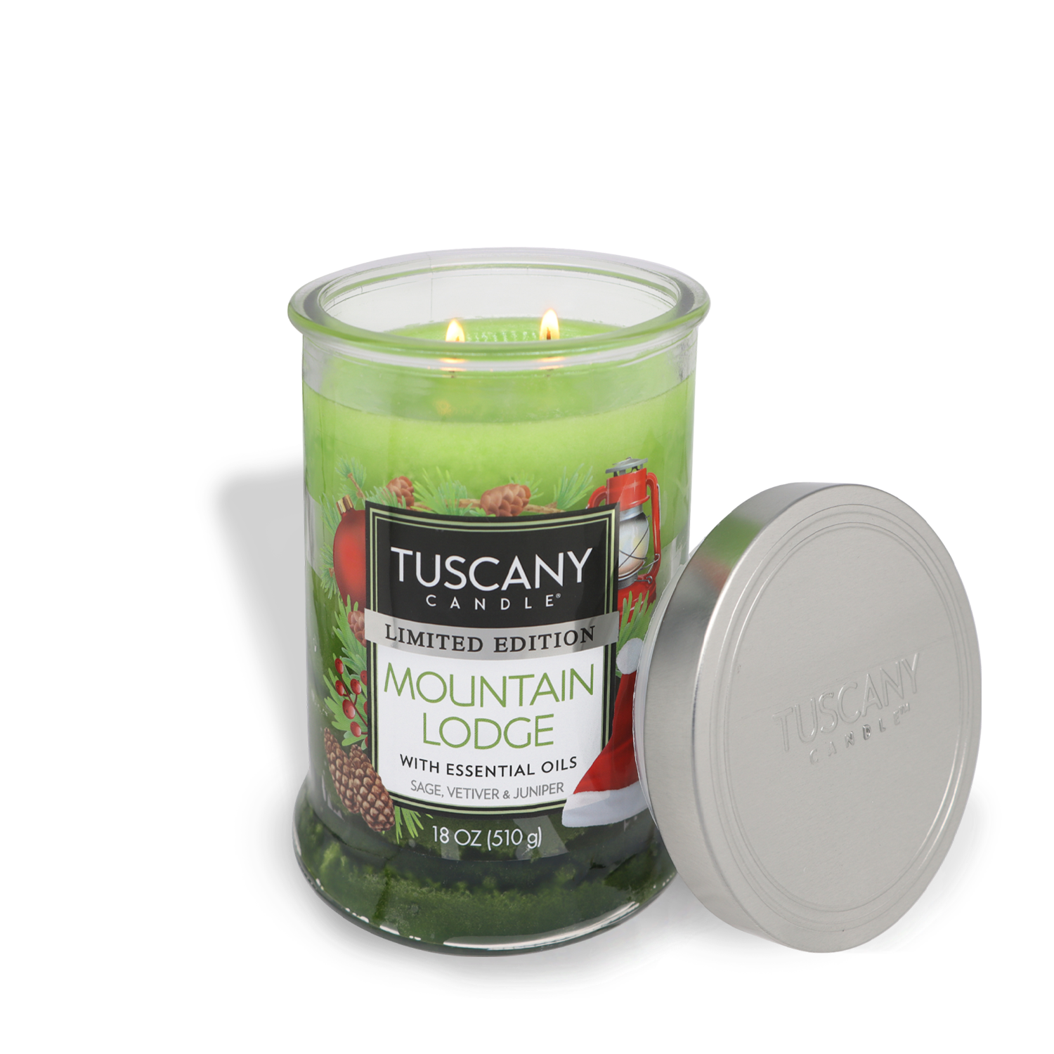 A lit "Mountain Lodge" Tuscany Candle® SEASONAL in an 18 oz (510 g) glass jar, featuring green wax and essential oils of sage, vetiver, and juniper, with its silver lid resting beside it.