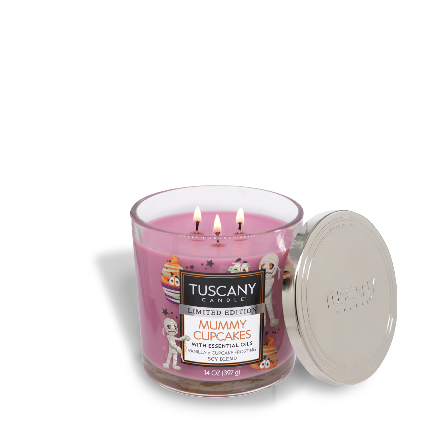 Pink Tuscany Candle in a glass jar labeled "Mummy Cupcakes," featuring mummy-themed cupcakes. Made with premium satin wax, the Mummy Cupcakes Long-Lasting Scented Jar Candle (14 oz) by Tuscany Candle® SEASONAL has three lit wicks and a silver metal lid resting beside it.