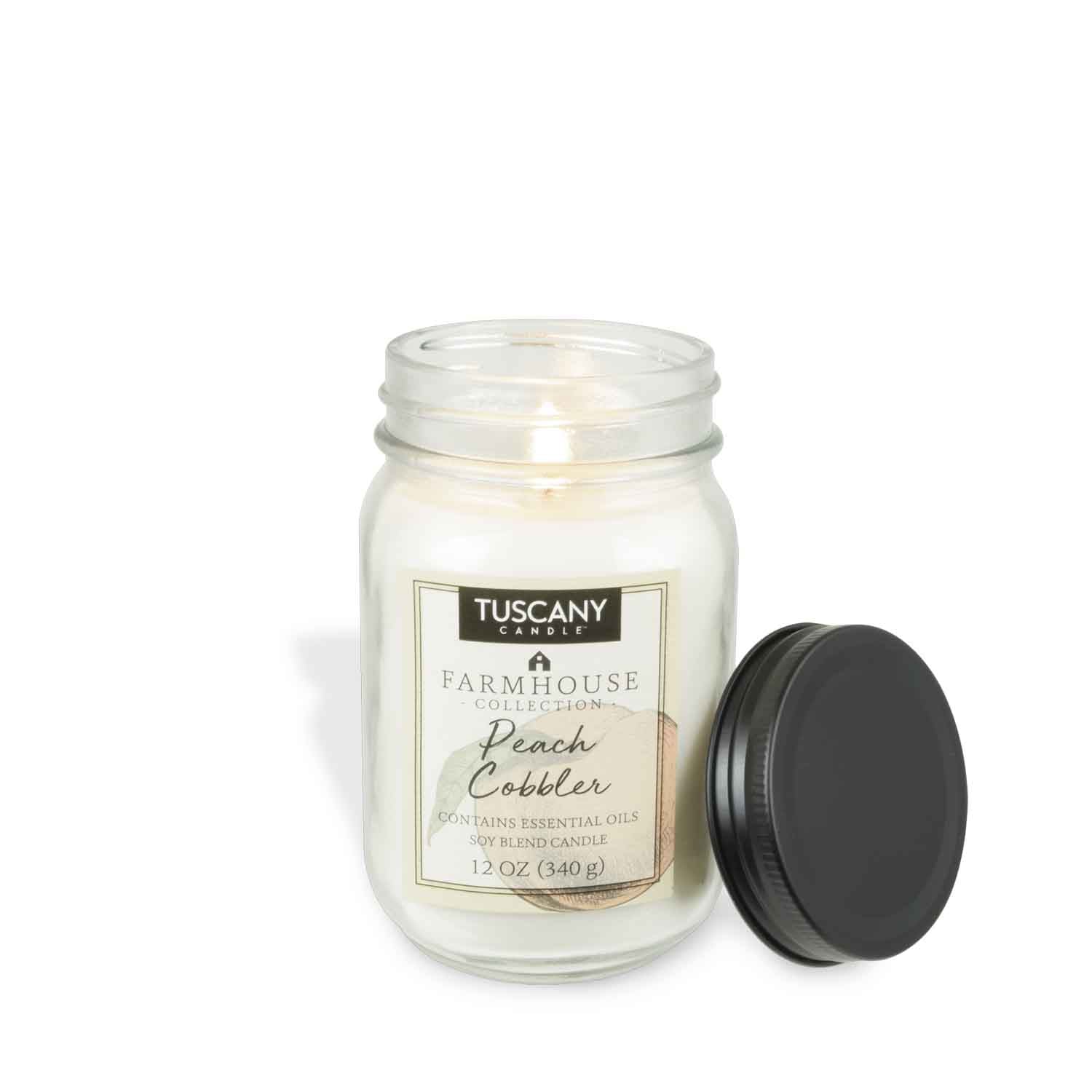 A Tuscany Candle® EVD from the Farmhouse Collection sits in a glass jar, labeled "Peach Cobbler." With sweet peach and brown sugar essence, its lid rests aside, radiating a cozy ambiance.