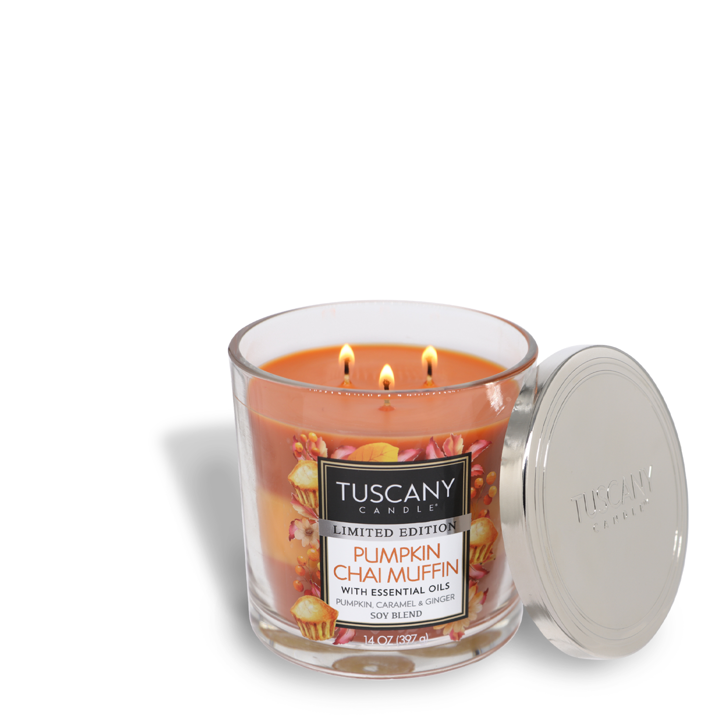 A lit Tuscany Candle® SEASONAL in a glass jar with a silver lid, labeled "Pumpkin Chai Muffin Long-Lasting Scented Jar Candle (14 oz)." This 14 oz scented jar candle, featuring three wicks, pampers your senses with fragrant notes and boasts a burn time of 50 hours.