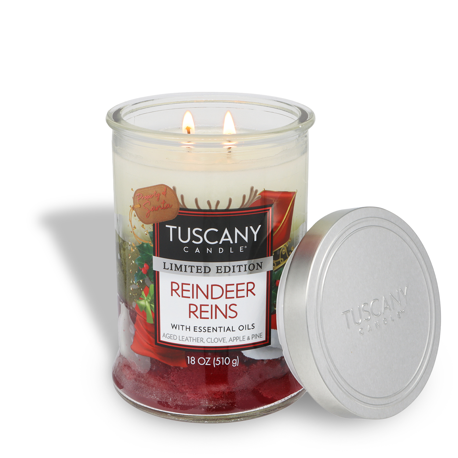 An 18 oz Tuscany Candle® SEASONAL jar labeled "Reindeer Reins: Aged Leather & Pine," features two lit wicks and a silver lid beside it. This limited edition holiday candle captures a festive scent.