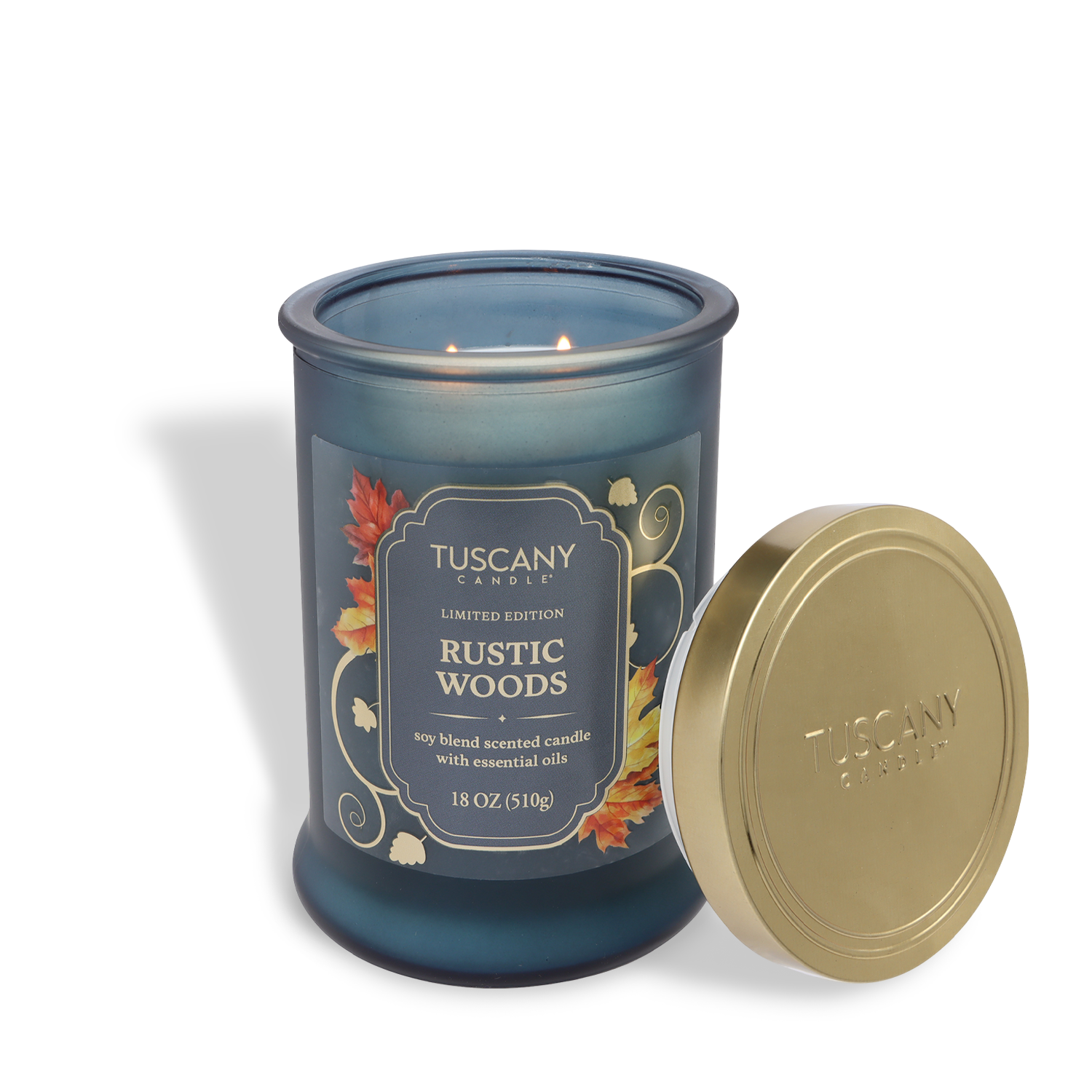 An 18 oz Tuscany Candle® SEASONAL “Rustic Woods: Sandalwood & Vanilla Scented Fall Candle” with autumn leaf designs and a blue glass jar sits beside its gold lid.
