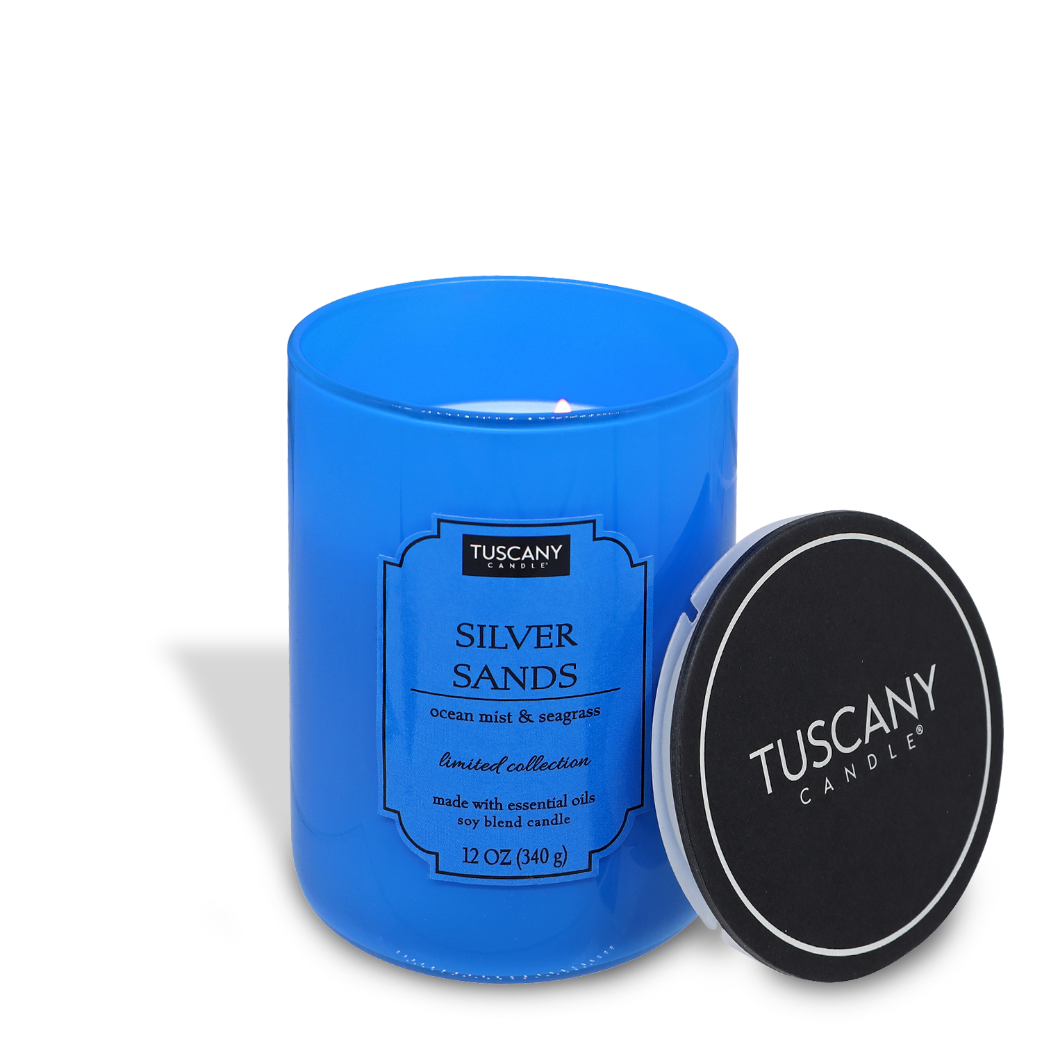 A lit blue "Silver Sands candle" with an open black lid lying next to it, on a white background.