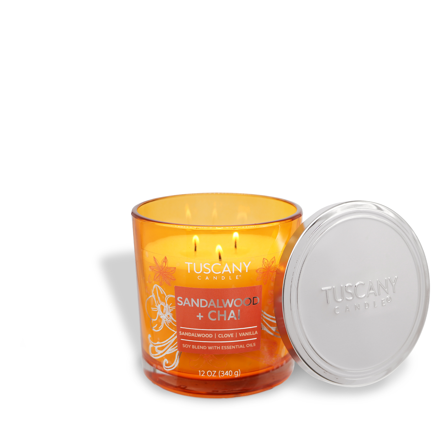 A lit orange jar candle labeled "Sandalwood + Chai: Vanilla Bean Scented Jar Candle (12 oz)" from the Painters' Palette Collection by Tuscany Candle® EVD has a silver lid leaning against it.