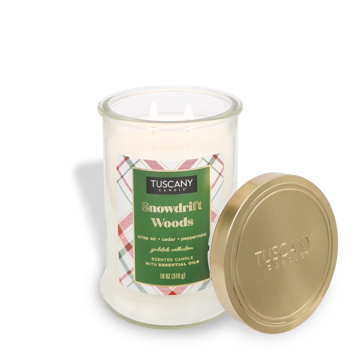 An 18 oz lit "Snowdrift Woods" scented jar candle from the Tuscany Candle® SEASONAL Winter Flannels Collection sits beside its gold lid, featuring a label that reads "crisp air, cedar, peppermint" and essential oils.