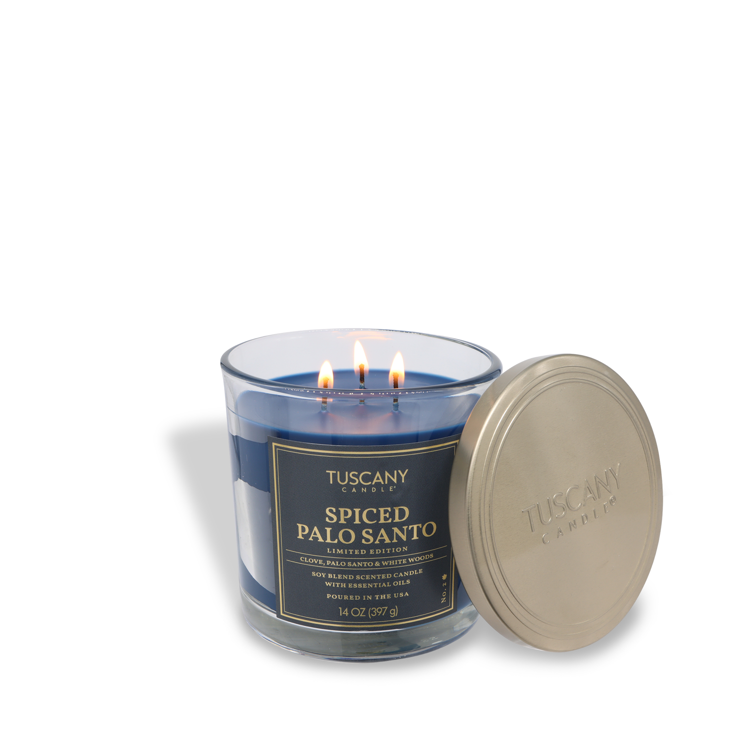 A Tuscany Candle® SEASONAL Spiced Palo Santo: Patchouli & Clove Scented Fall Candle (14 oz) burns with three flames in a clear glass jar, its gold lid resting beside it.