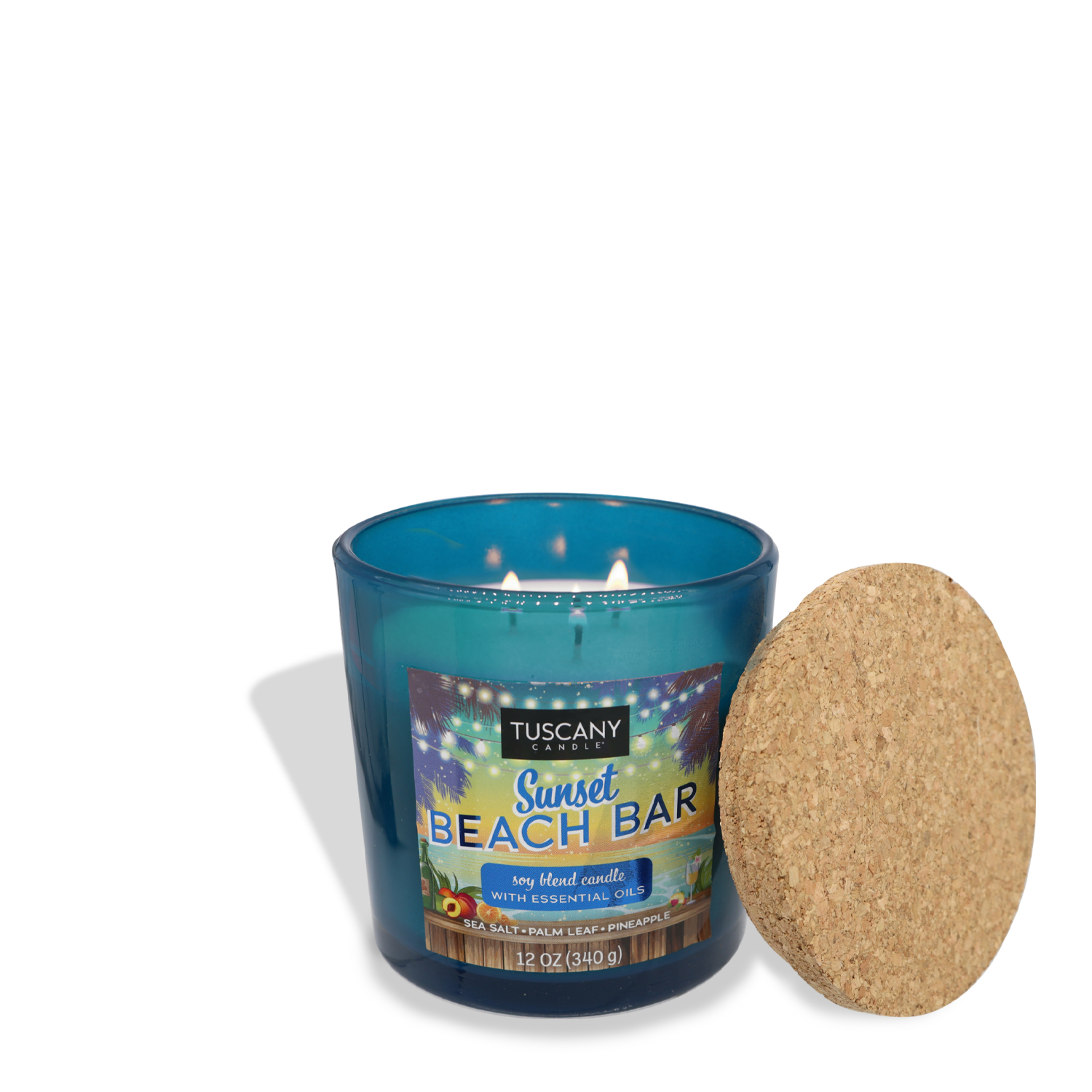 A blue Tuscany Candle® SEASONAL labeled "Sunset Beach Bar (12 oz) – Sunset Beach Bar Collection" with three lit wicks, exuding a hint of sea salt and coconut water. The cork lid lies flat beside the candle.