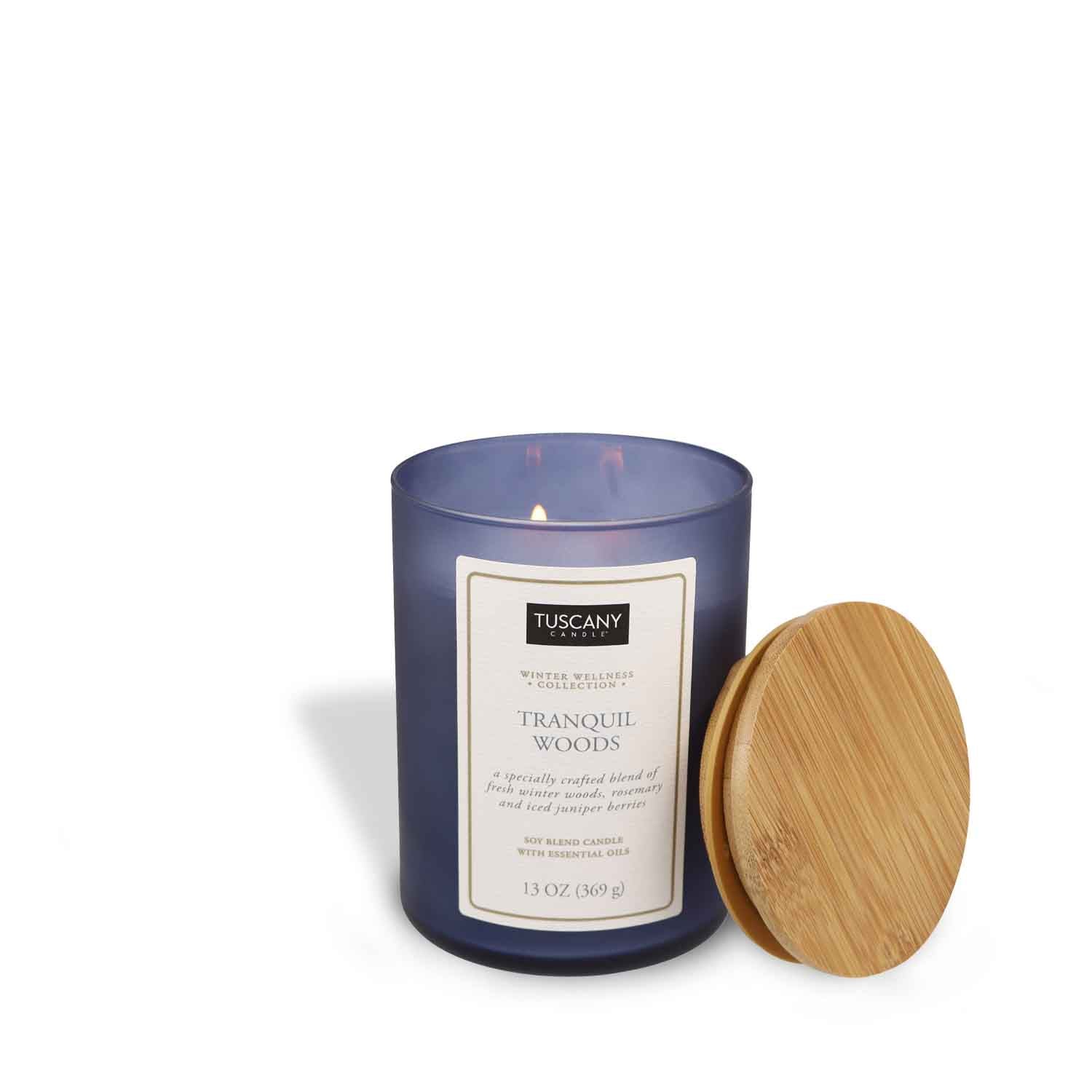 A Tranquil Woods Scented Jar Candle (13 oz) – Winter Wellness Collection by Tuscany Candle with a wooden lid next to it.