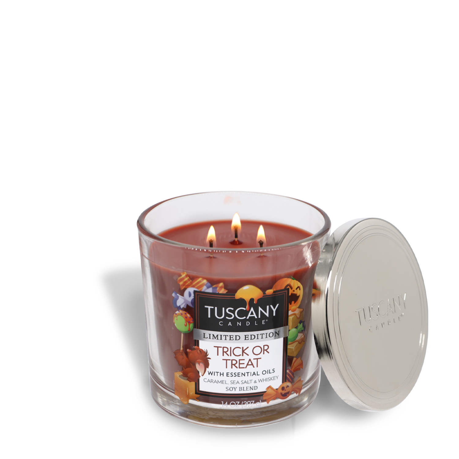 A Trick Or Treat Long-Lasting Scented Jar Candle (14 oz) by Tuscany Candle® SEASONAL with three lit wicks in a glass container. The label reads "Limited Edition Trick or Treat with Essential Oils: Caramel, Sea Salt and Whiskey - Soy Blend." This premium satin wax candle showcases exquisite fragrance notes, with the lid placed beside it.