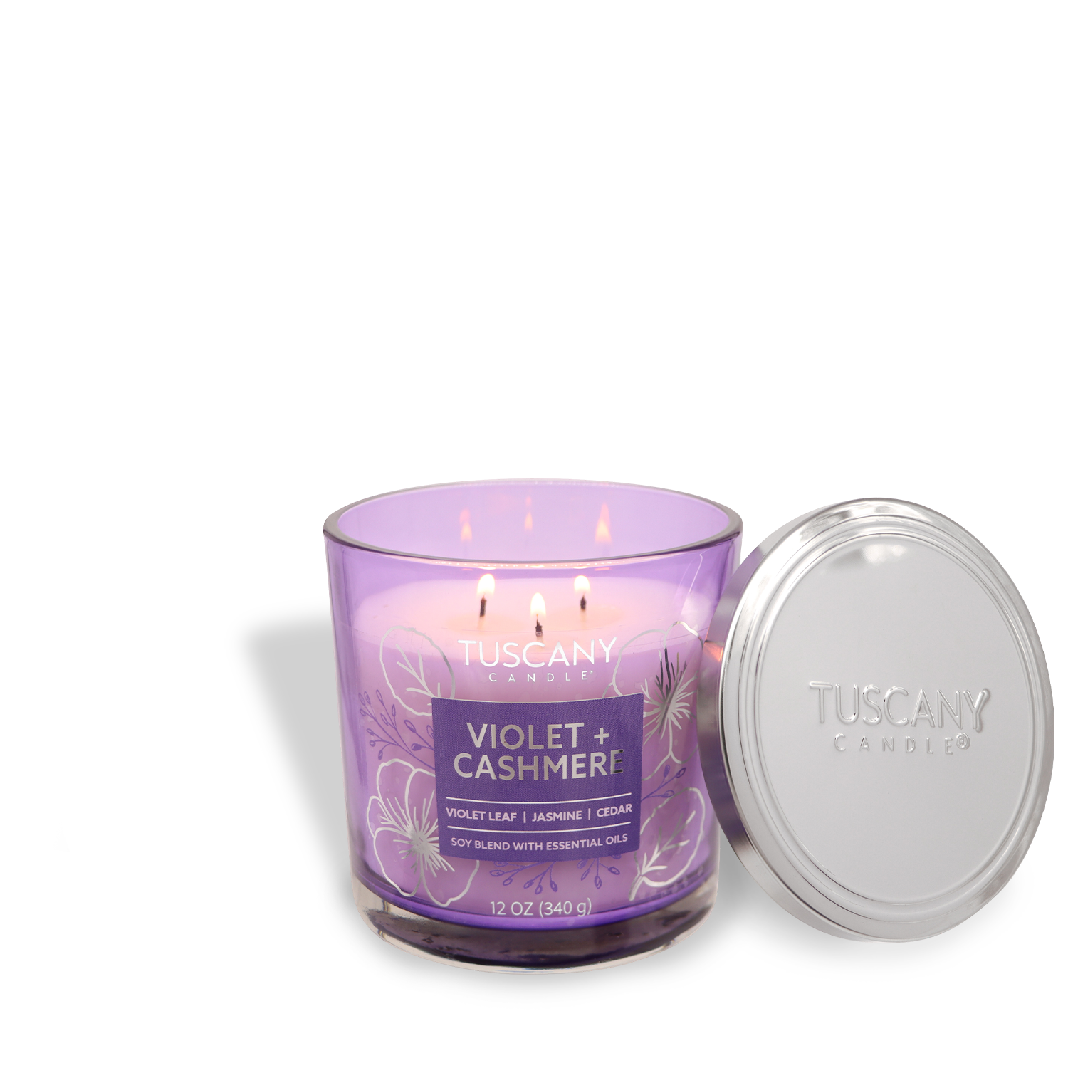 A 12 oz jasmine-scented jar candle from Tuscany Candle® EVD's Painters' Palette Collection, labeled "Violet + Cashmere," features lit wicks and sits next to a silver lid.