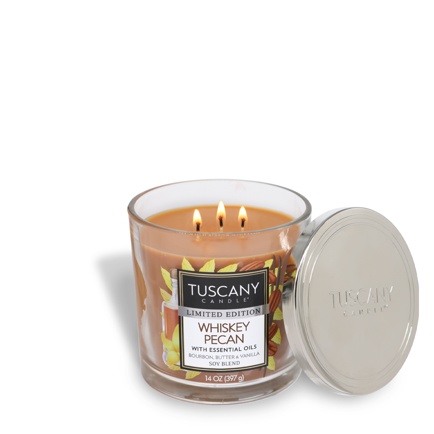 A Tuscany Candle® SEASONAL Whiskey Pecan Long-Lasting Scented Jar Candle (14 oz) with three wicks, partially lit, and a metal lid placed to the side. The candle label indicates it is a limited edition with essential oils and premium satin wax.