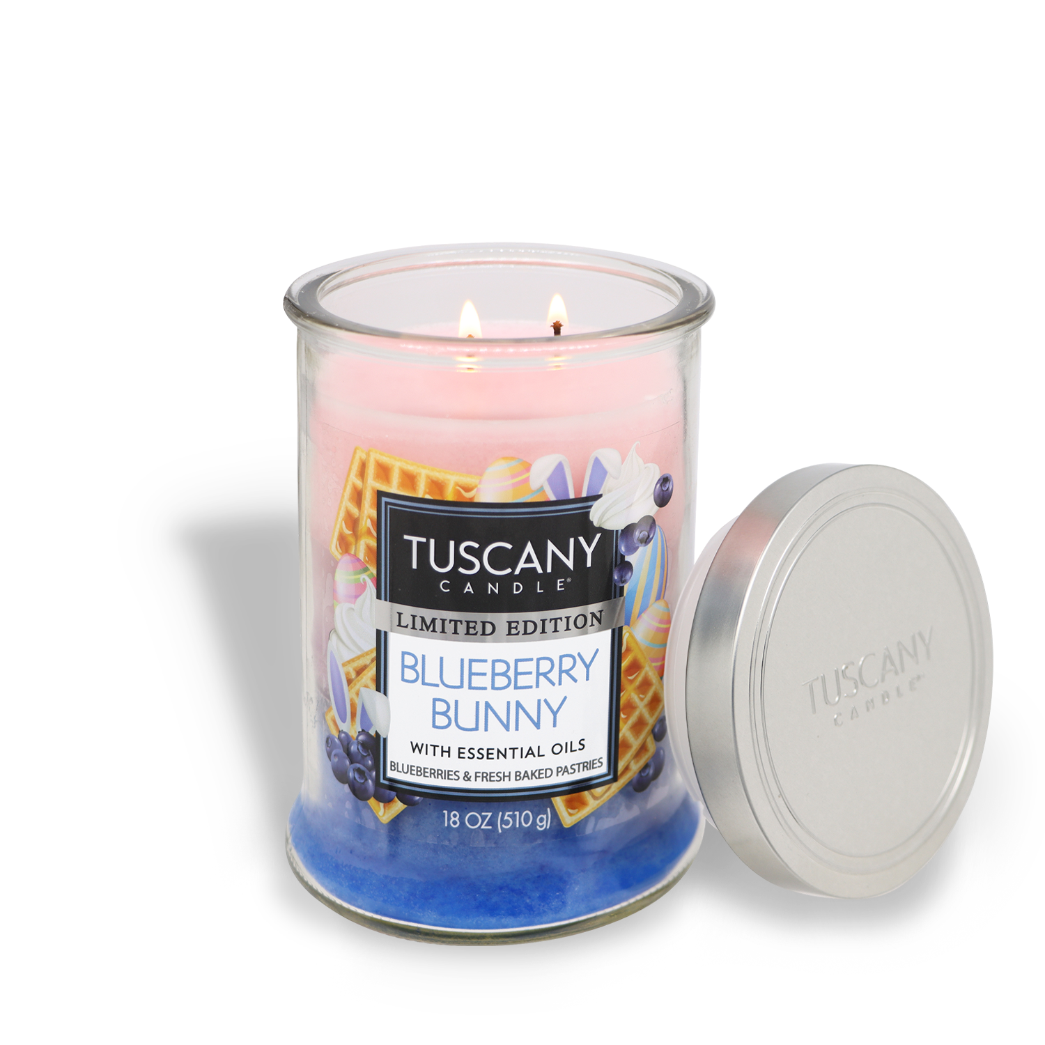 A Tuscany Candle® SEASONAL "Blueberry Bunny" Easter candle is lit; it's two-wicked, waffle-scented, in an 18 oz glass jar with its silver lid beside it.