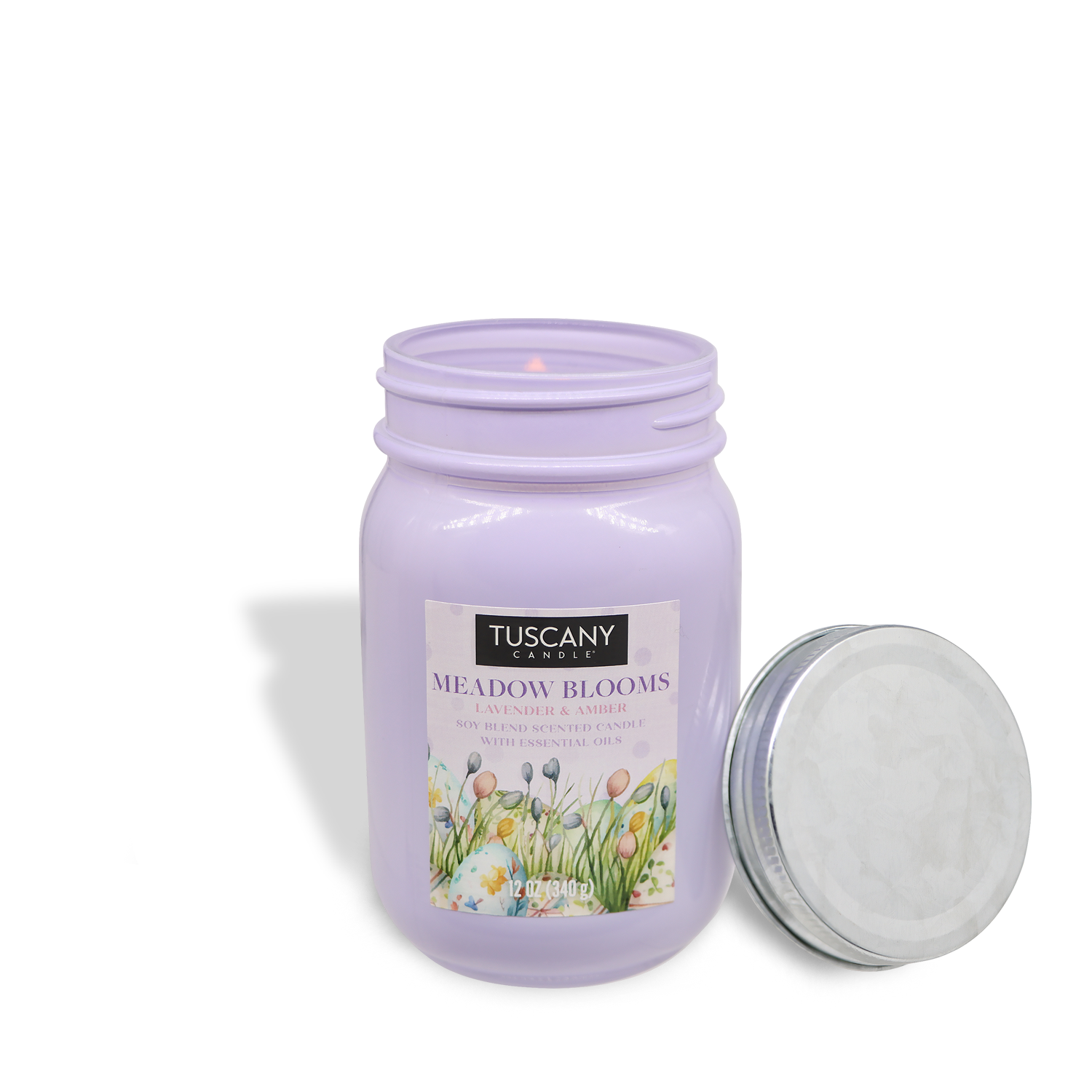 The Tuscany Candle® SEASONAL product "Meadow Blooms: Lavender Scented Easter Candle," a 12 oz lavender and amber-scented candle, is shown with the lid placed next to the lavender candle jar.