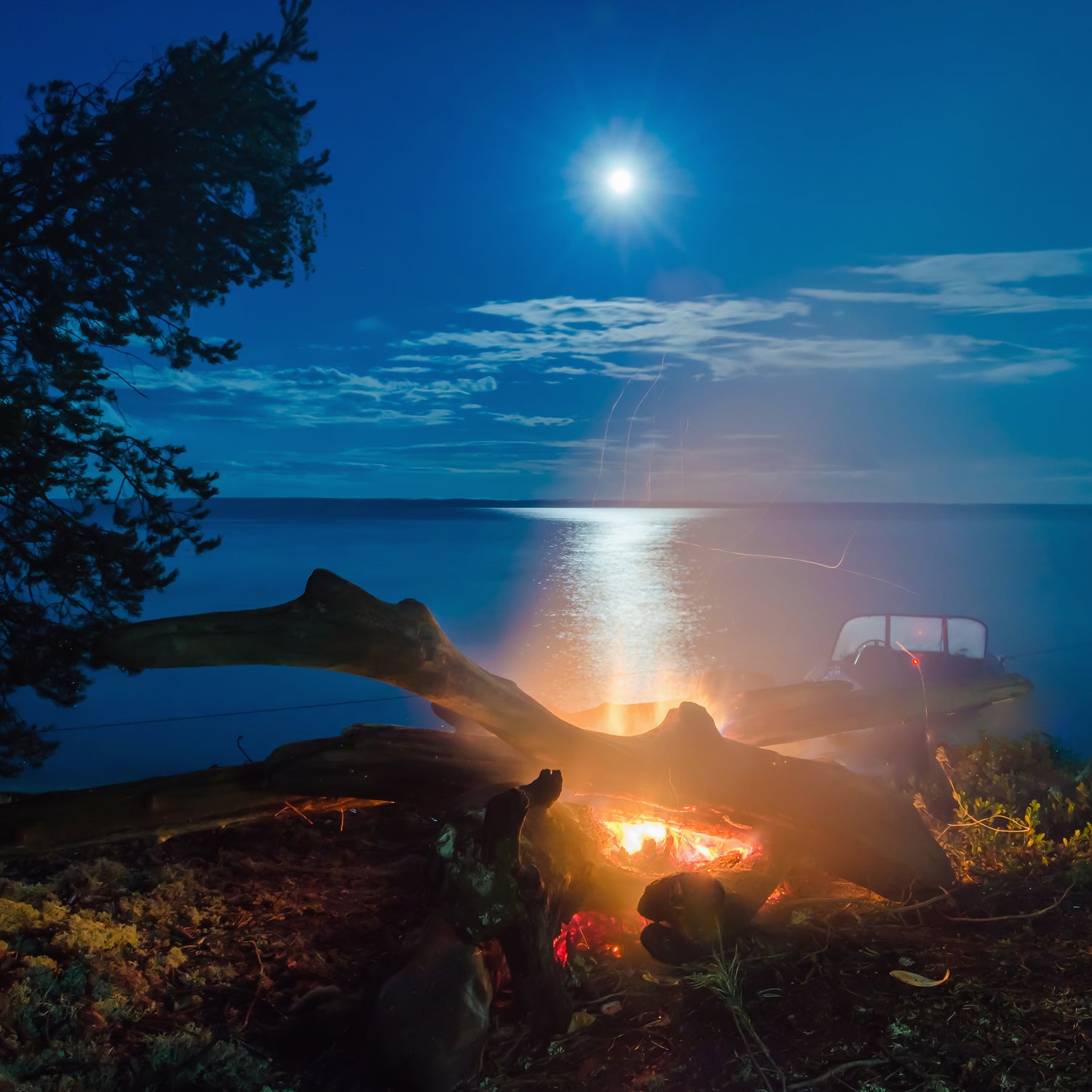 A Evening Fireside Long-Lasting Scented Jar Candle (14 oz) by Tuscany Candle, with a woodsy fragrance, flickering glow, and a full moon reflecting on a lake at night.