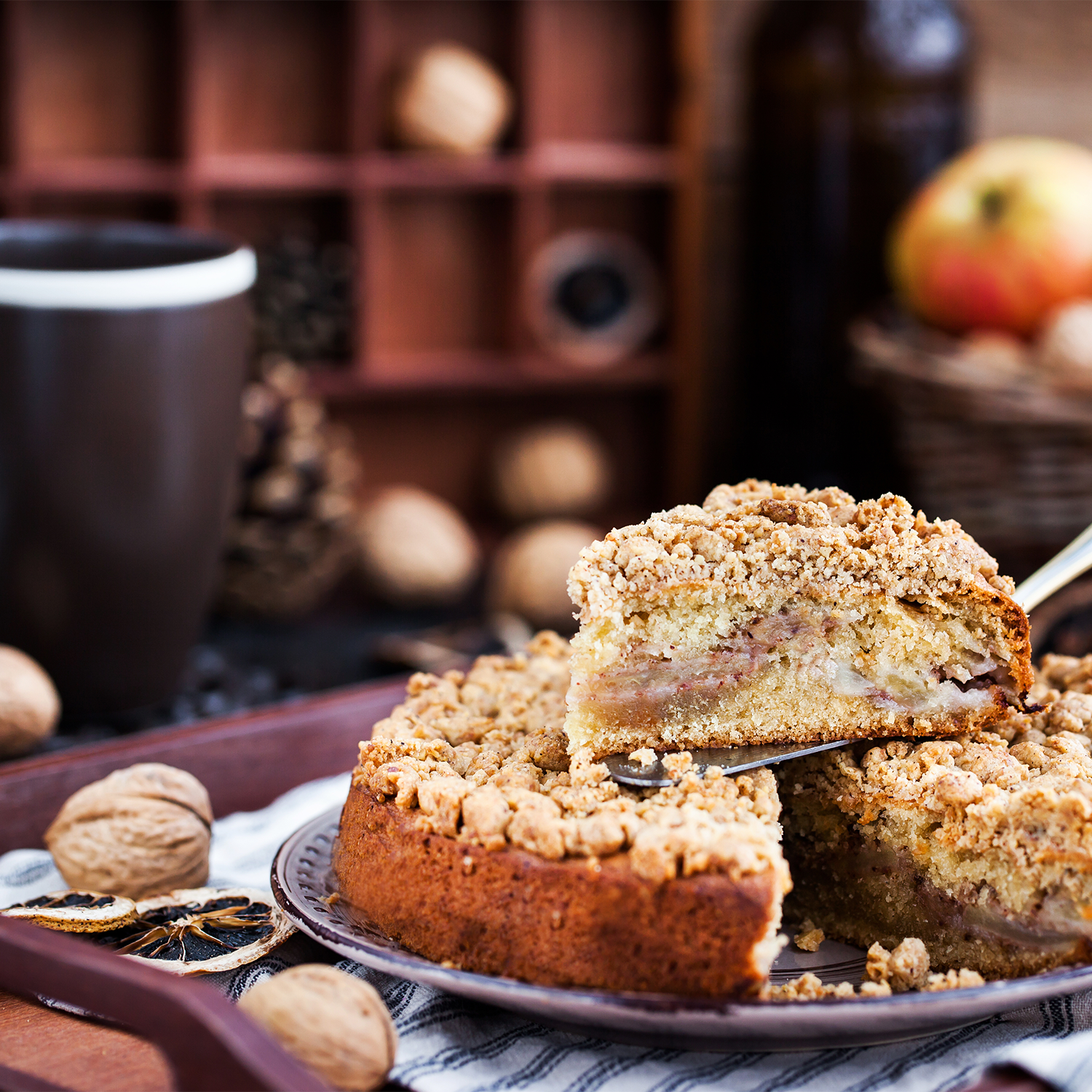 A still life photo of a slice of coffee cake with a crumble topping. This cake is the inspiration for the "Cinnamon Coffee Cake" scented candle from Tuscany candle