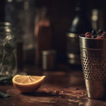 Load image into Gallery viewer, A still life photo of a masculine bar top showing  citrus and herbs, some of the key fragrance notes in the &quot;Citrus and Peppercorn&quot; scented candle from Tuscany Candle&#39;s &quot;Homme &amp; Heritage&quot; collection of manly candles
