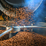 Load image into Gallery viewer, A photo of roasting coffee beans in the hopper of a coffee roaster. Coffee is one of the main fragrance notes in the &quot;Cafe au Lait&quot; candle from Tuscany candle.
