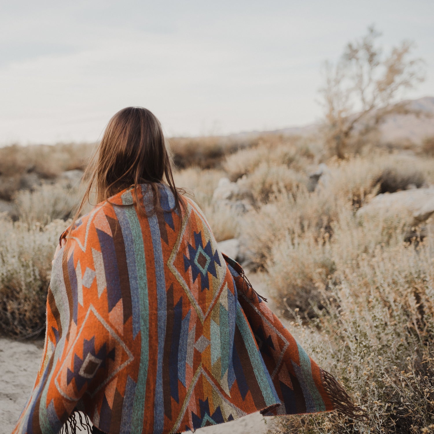 A meditative photo of a woman wrapped in a blanked on a tranquil desert morning. This photo inspires Tuscany Candle's Fragrance "Desert Detox"