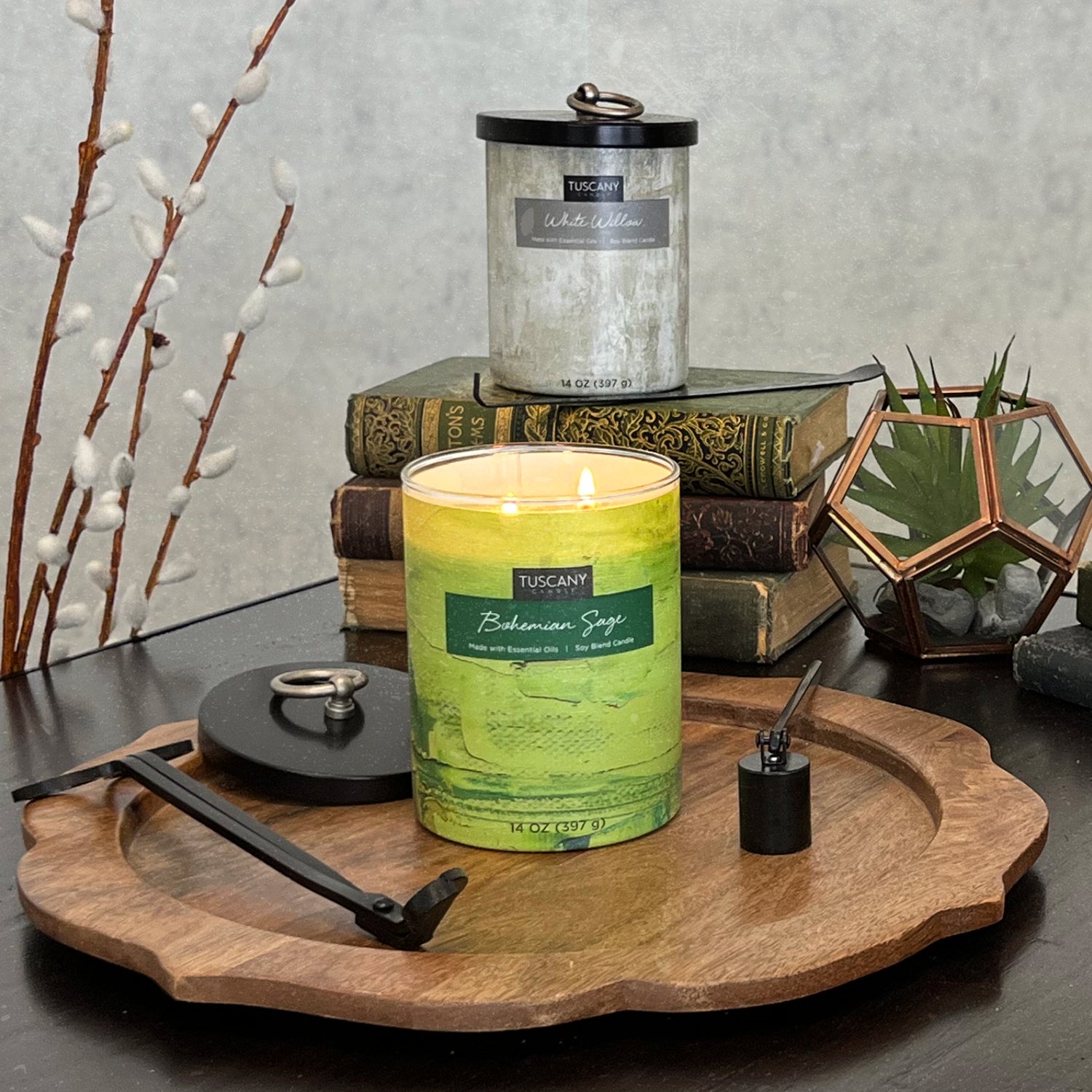 A White Willow Scented Jar Candle (14 oz) from Tuscany Candle sits on a wooden tray next to books, enhancing home décor.