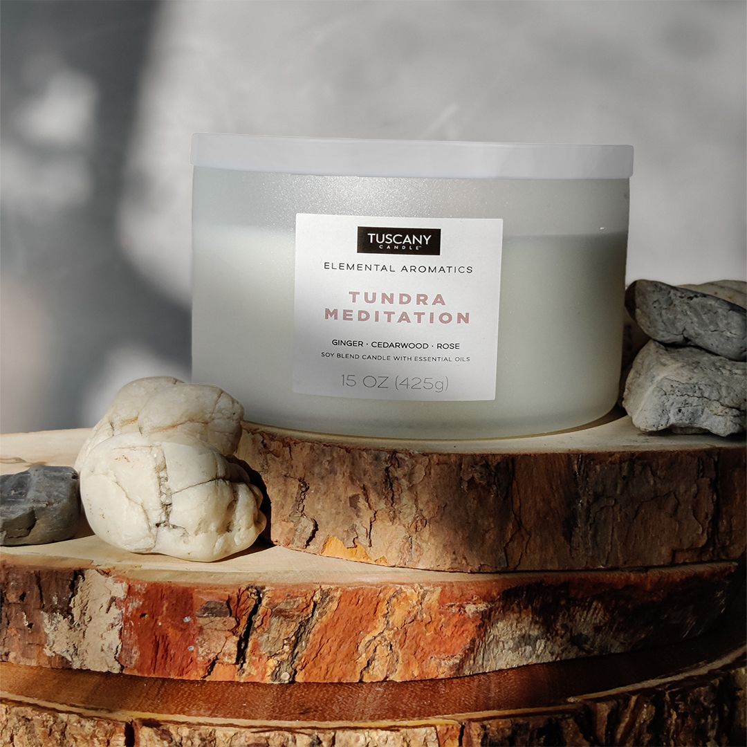 A Tundra Meditation scented jar candle (15 oz) from the Elemental Aromatics Collection by Tuscany Candle sitting on top of a log, creating a tranquil atmosphere for Tundra Meditation.