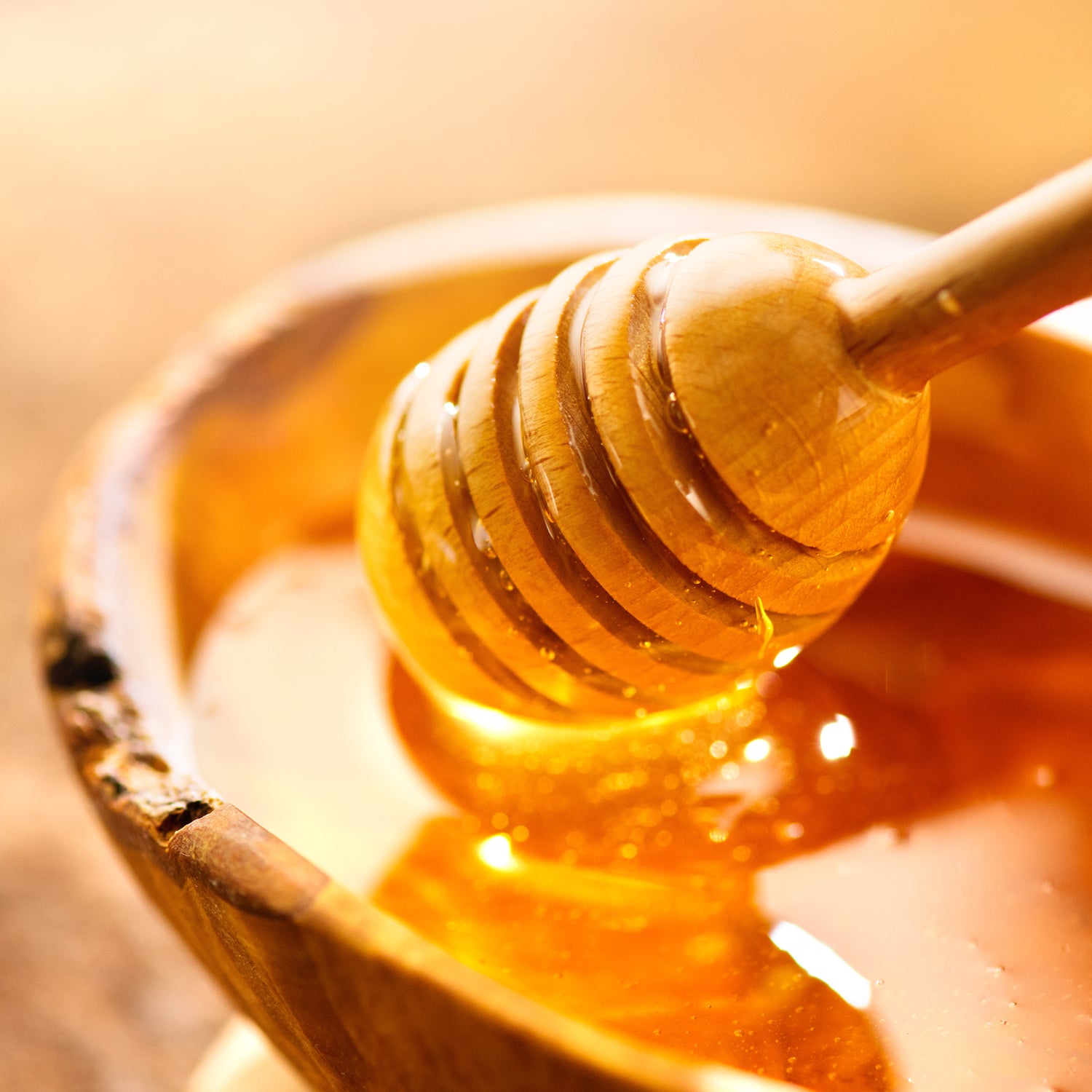 A wooden dipper in a bowl of honey, perfect for drizzling on Homemade Muffins Scented Jar Candle (12 oz) – Farmhouse Collection by Tuscany Candle® EVD or using as a sweetener in candle-making.