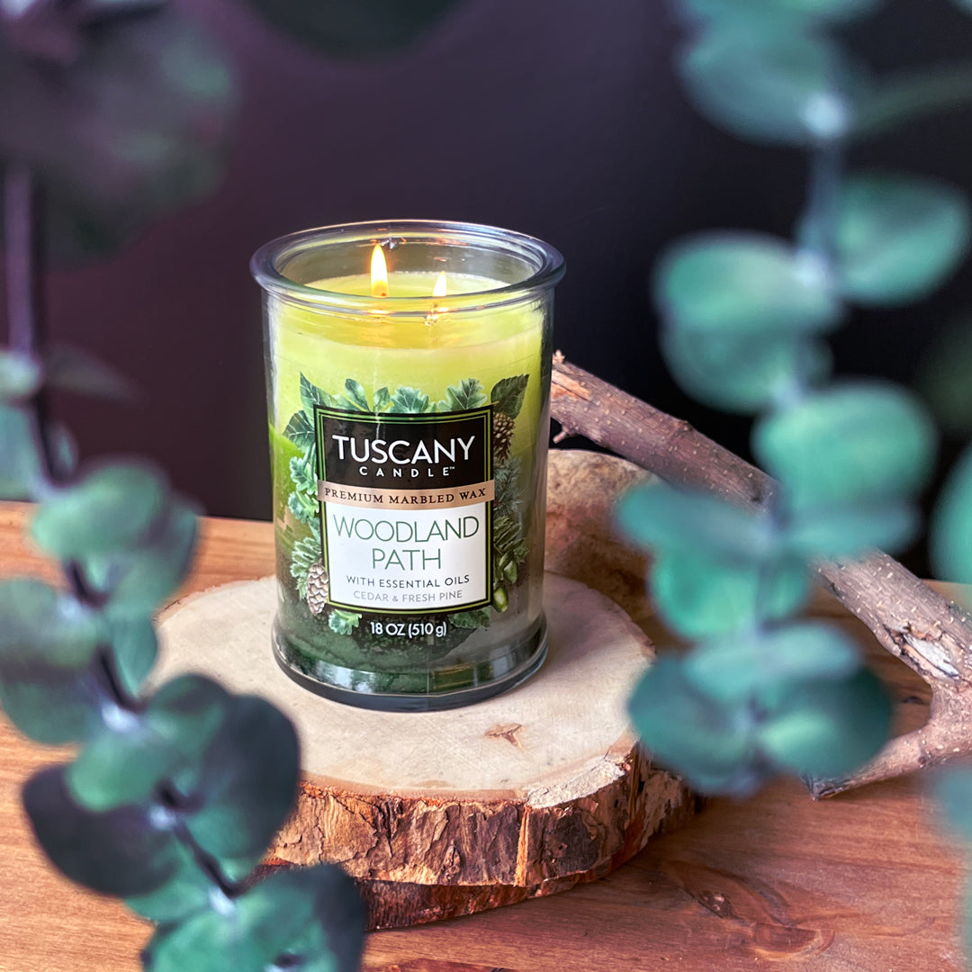 A Woodland Path Long-Lasting Scented Jar Candle (18 oz) from Tuscany Candle® EVD sitting on top of a piece of wood.