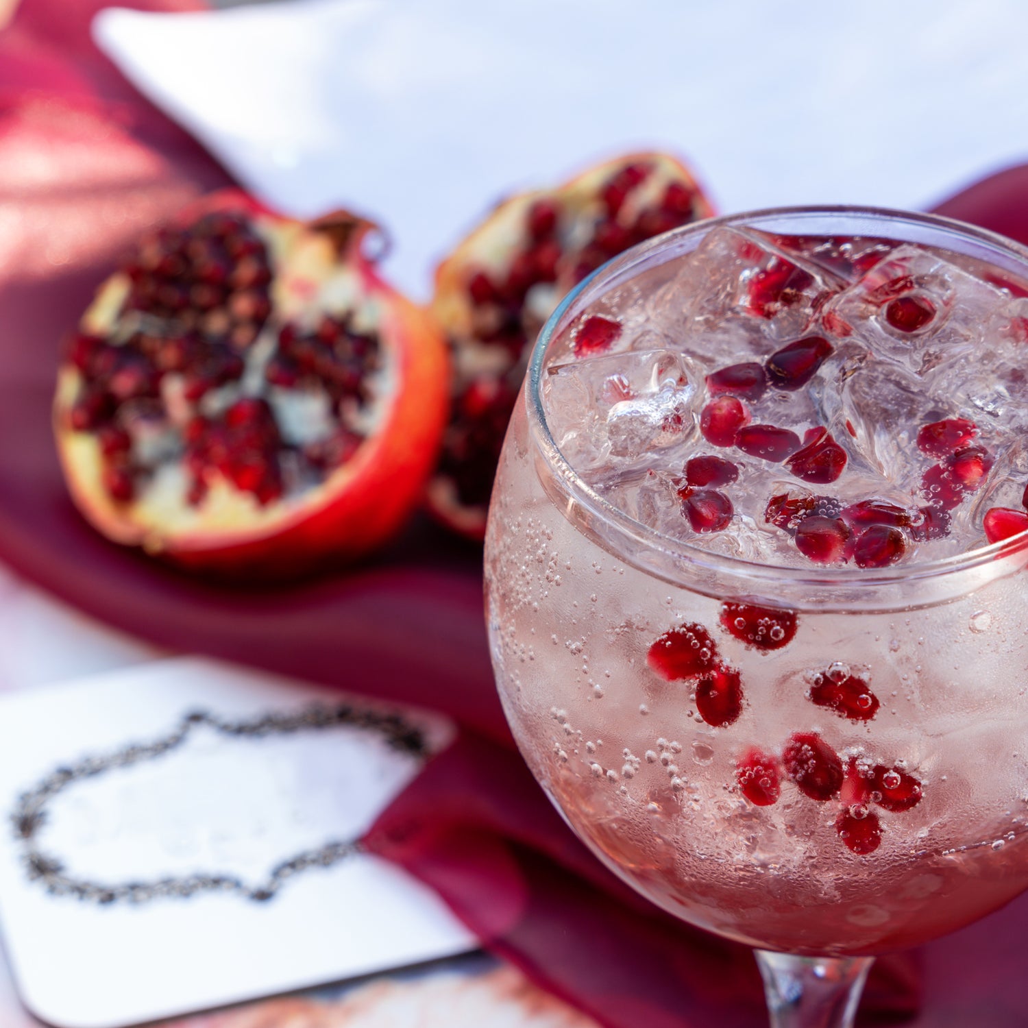 A glass of pomegranate cocktail with ice and Tuscany Candle's Pomegranate Fizz Long-Lasting Scented Jar Candle (14 oz).