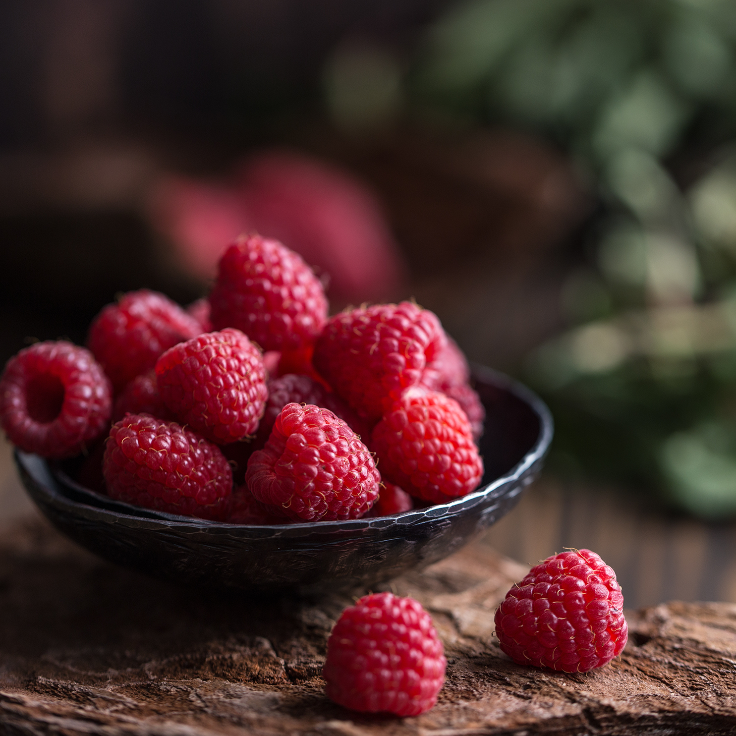 A bowl of fresh Raspberry & Sandalwood (12 oz) from the Tuscany Candle® EVD collection on a rustic wooden surface with soft, blurred greenery in the background.