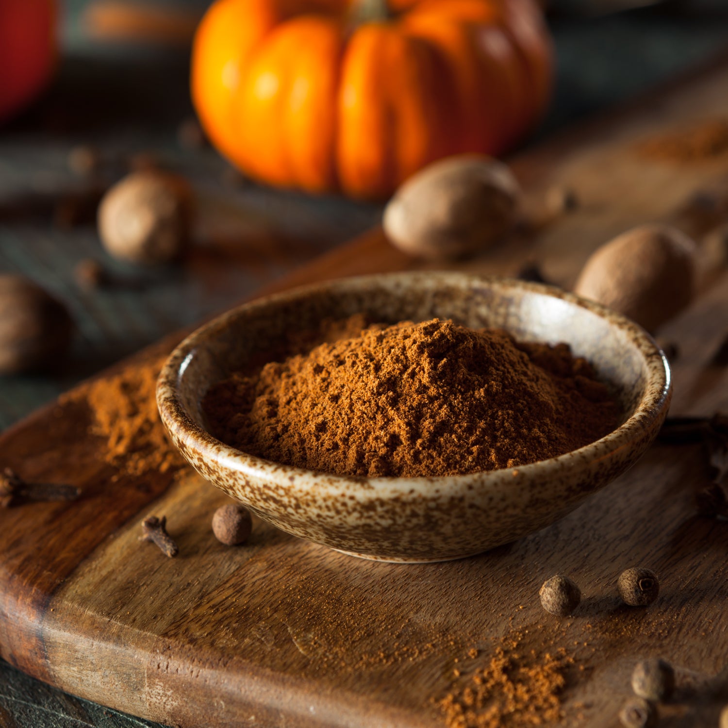 Tuscany Candle's Spiced Pumpkin Long-Lasting Scented Jar Candle (14 oz) with cinnamon and clove fragrance notes in a bowl on a wooden cutting board.