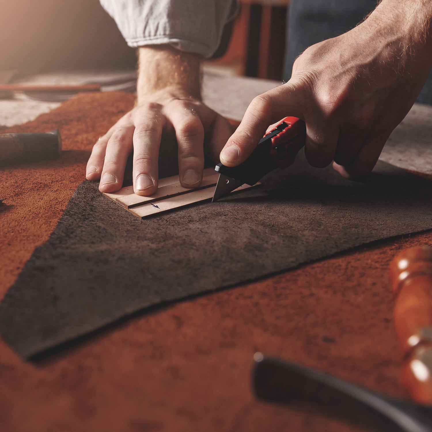 A leatherworker cuts suede, one of the inspirations for our Mahogany Suede scented wax melt bar