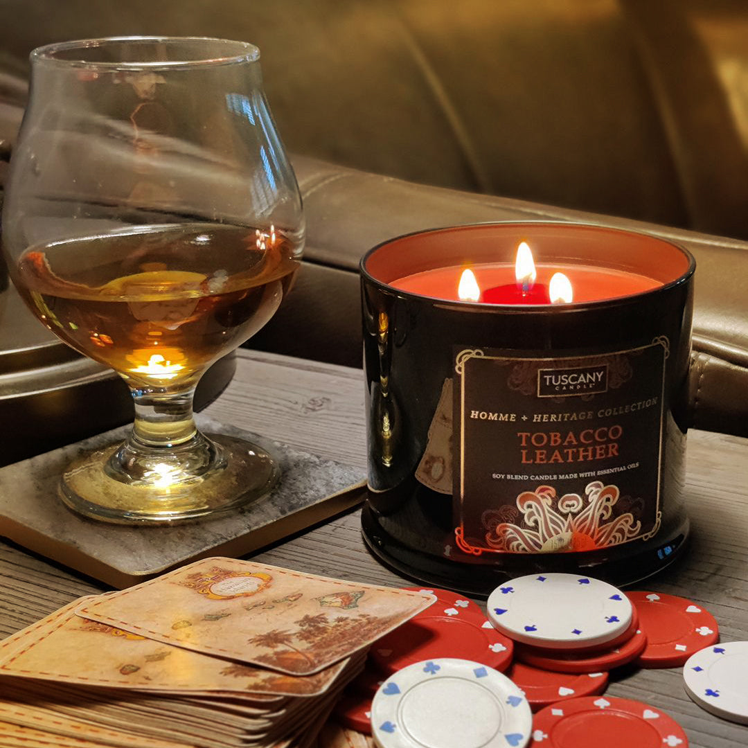 A tobacco Leather scented candle from Tuscany Candle sits on a poker table next to a glass of neat whiskey