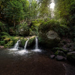 Load image into Gallery viewer, A photo of a woodland waterfall pouring into a bubbling creek. This scene is the inspiration for &quot;Woodland Waterfall&quot;, a unisex  scented candle from Tuscany Candle which seamlessly blends the invigorating essence of Fresh Ocean Air with the earthy undertones of Weathered Driftwood and a hint of Vetiver
